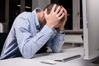 パソコンの画面の前で頭を抱えてうつむく男性